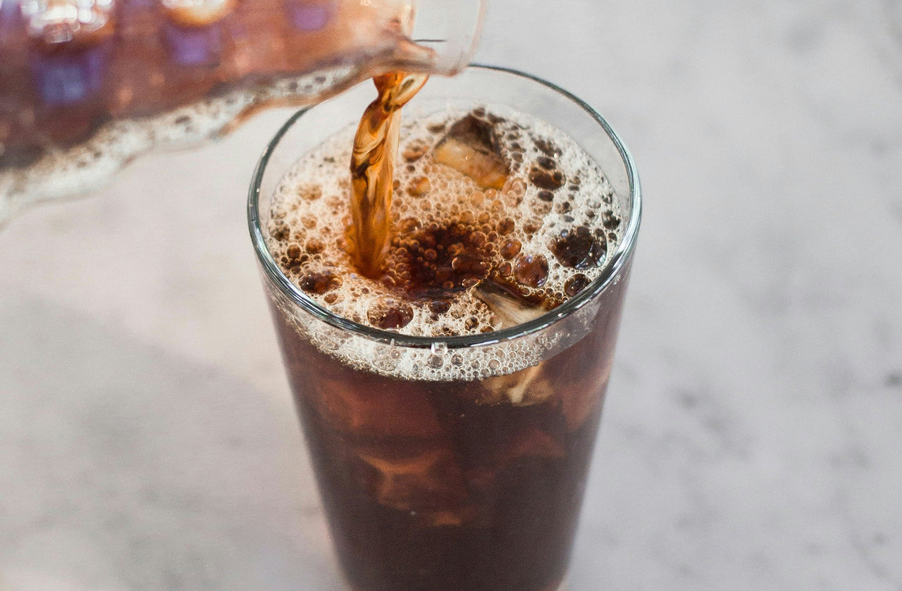 Cold brew coffee being poured over ice in a tall glass
