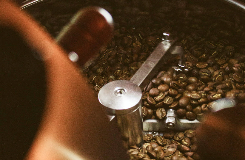 A close-up of freshly roasted coffee beans in a coffee roaster drum with a stirring arm