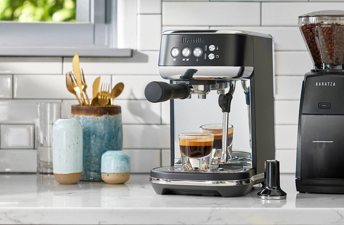 Breville Bambino Plus pulling two espresso shots beside a Baratza grinder on a tiled counter