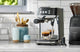 Breville Bambino Plus pulling two espresso shots beside a Baratza grinder on a tiled counter