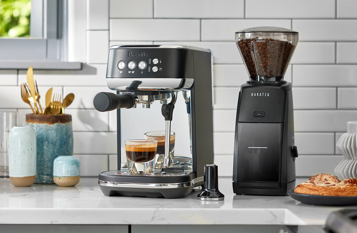 Black Breville espresso machine and Baratza grinder on a marble kitchen counter - Seattle Coffee Gear