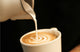Steamed milk pouring from a pitcher into a latte with rosetta art