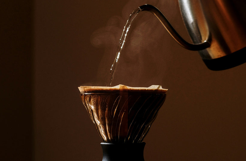 A kettle pouring hot water into a pour over coffee maker