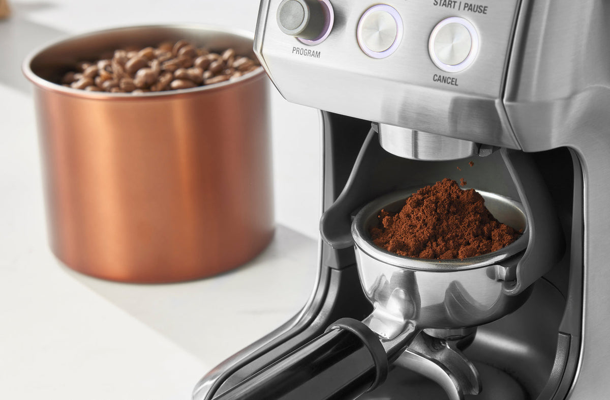 Fine espresso grind dosing into a portafilter from a burr grinder beside copper bean canister - Seattle Coffee Gear