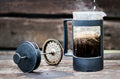 A disassembled French press plunger next to a carafe of coffee with steam rising