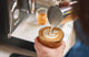 Barista pouring steamed milk with latte art into a glass espresso cup at a home machine