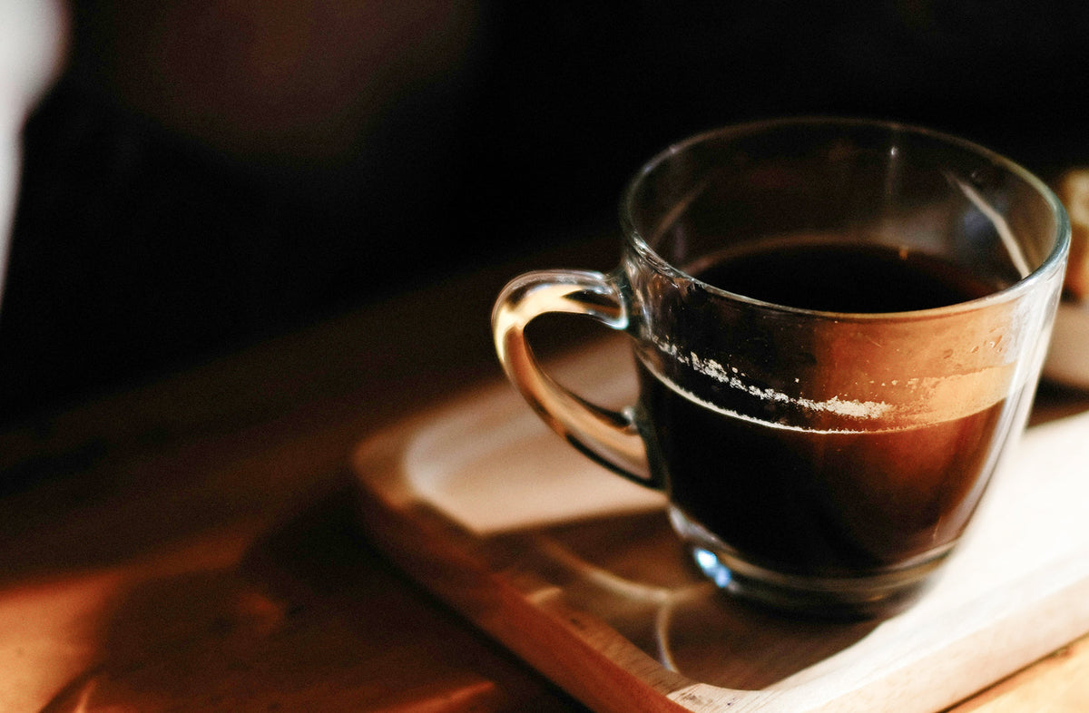 Glass cup of dark decaf espresso with crema on a wooden tray - Seattle Coffee Gear