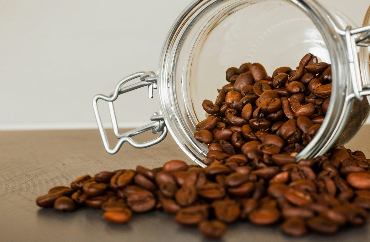 Roasted coffee beans spilling from an airtight glass storage canister