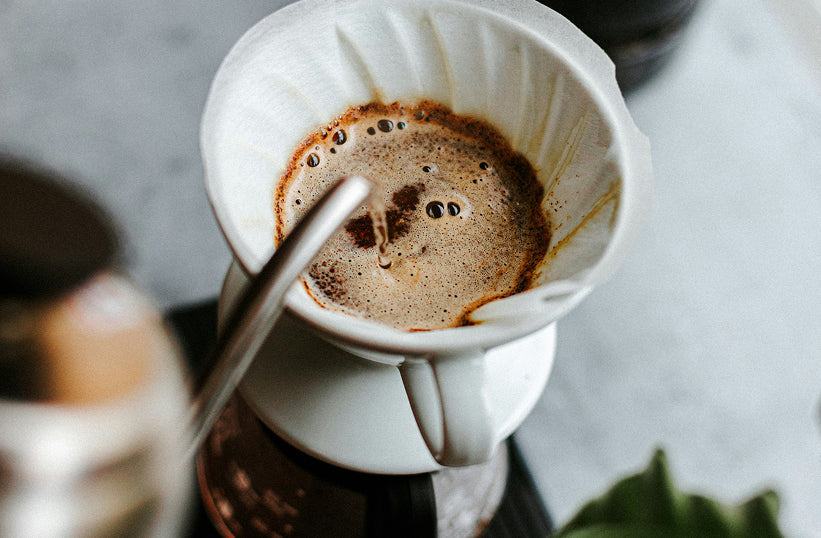 Hot water being poured from a gooseneck kettle into a pour over dripper showing coffee bloom