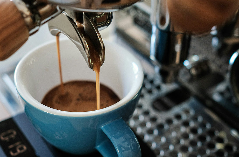 A double espresso shot pouring into a blue ceramic cup on a scale
