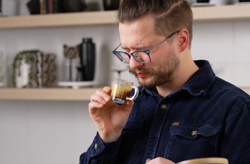 Barista smelling a shot of light roast espresso in a glass cup - Seattle Coffee Gear
