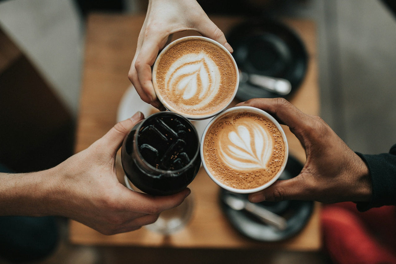 Three coffee cups being clinked together, two with latte art and one ice. Photo by Nathan Dumlao on Unsplash       