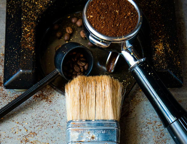 Espresso machine cleaning tools including a group head brush, portafilter with coffee grounds, and a knock box on a countertop - Seattle Coffee Gear